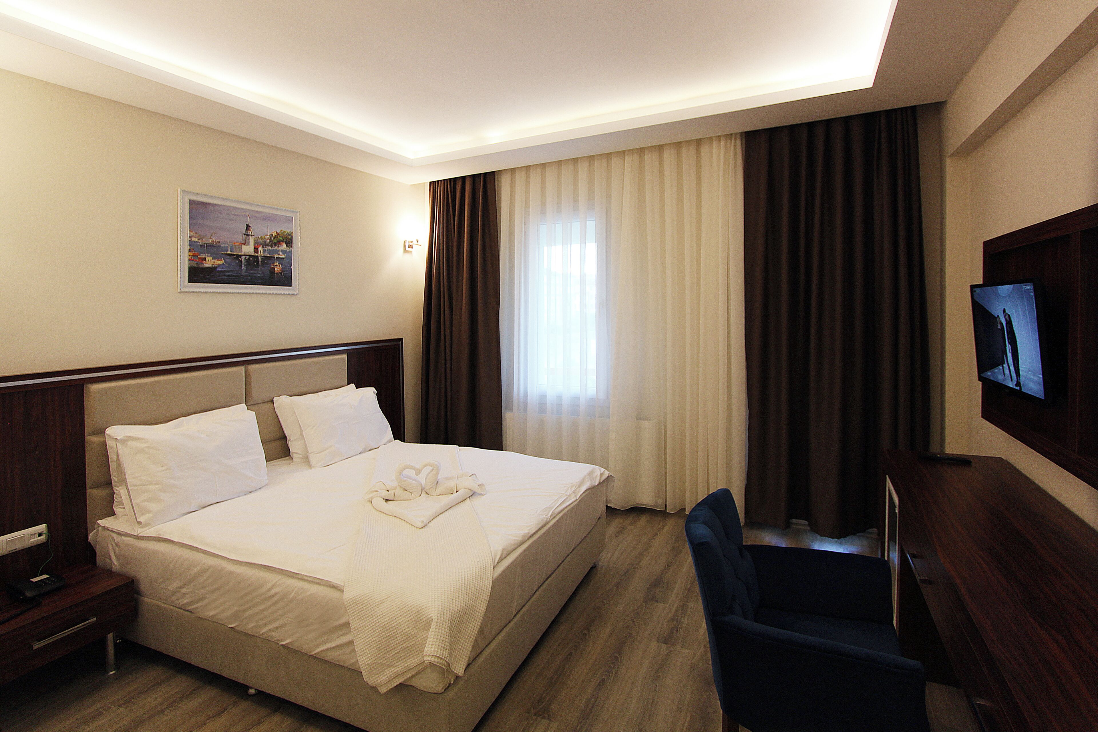 A hotel room with a bed, a desk, a chair, a TV, and a painting on the wall.. Yeşilhisar  Hotel