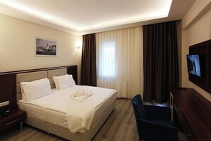 Habitación de hotel con cama, escritorio, silla, televisor y un cuadro en la pared.