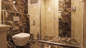 Een badkamer met toilet, een douche met glazen deur en marmeren tegels.