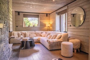 A cozy living room with a sectional sofa, a round coffee table, and a round mirror on the wall. - Exceptional 12P Chalet With Sauna and Jacuzzi (Megeve)