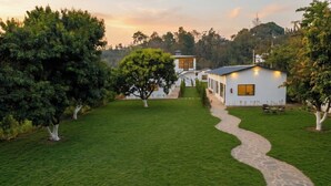 A pathway leading to a white building with a balcony, surrounded by trees and a grassy area. - Corbett Retreat (Kotabagh)
