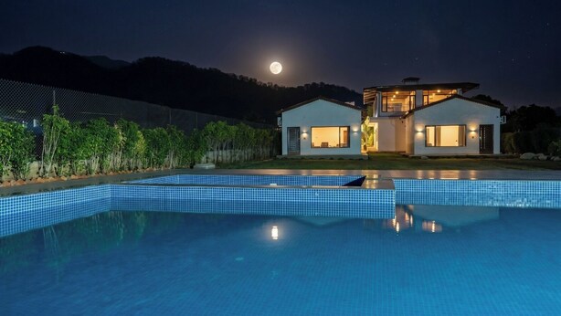 A modern house with a swimming pool, a moon in the sky, and a fence with greenery. - Corbett Retreat (Kotabagh)