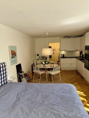 Un apartamento moderno con comedor, cocina y una cama con colcha estampada.