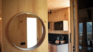 A wooden interior with a circular mirror, a kitchen area with a microwave, and a view through a glass door.