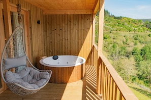 Een houten terras met een hangstoel en een jacuzzi.