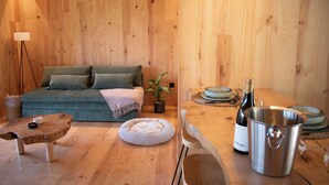 A wooden interior with a sofa, a small round table, a potted plant, a wine bottle, and a metal bucket.