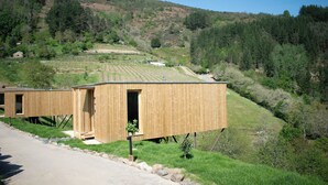 A wooden cabin with a small porch, situated on a hillside with a view of the surrounding forest.