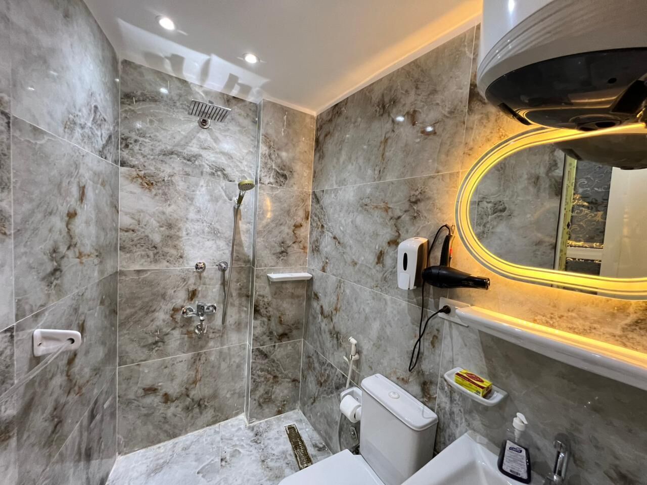 Een moderne badkamer met douche, toilet en wastafel, marmeren wanden en een spiegel met verlichte lijst.
