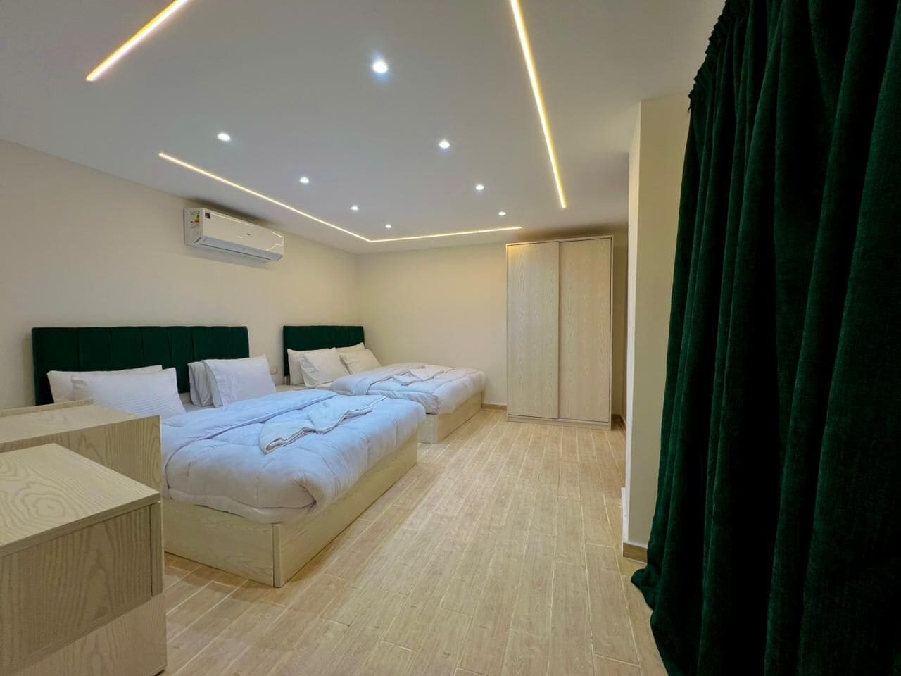 Ein Hotelzimmer mit zwei Betten, einem Schreibtisch, einem Kleiderschrank und einer Klimaanlage.
