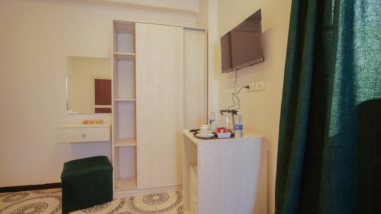 Ein Hotelzimmer mit Schrank, einem kleinen Tisch mit Toilettenartikeln, einem Spiegel und einem an der Wand befestigten Fernseher.