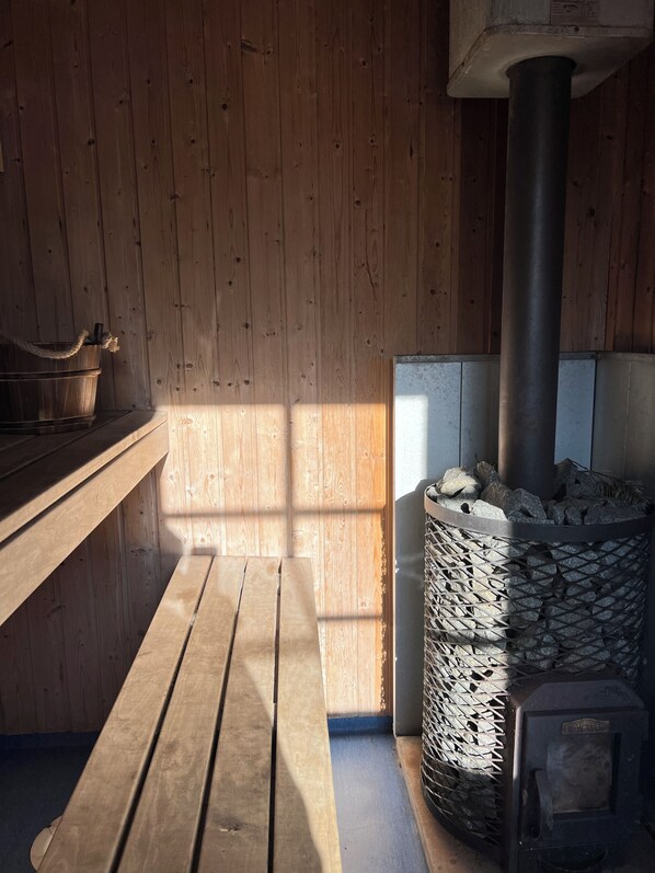 A wooden interior with a bench, a stone stove, and a metal container.