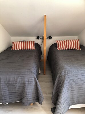 A room with two beds, each with striped pillows, a wooden central pole, and a ceiling-mounted lamp.