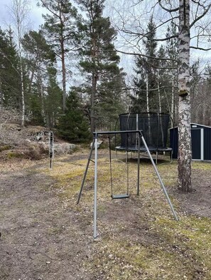A playground with swings and a trampoline, surrounded by trees.