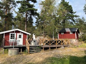 A red cabin with a porch and a chimney, a wooden deck, and a small bridge.