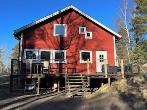 A red wooden house with a porch, two windows, and a door.