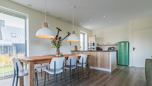 Una cocina moderna con una mesa de comedor de madera, sillas blancas, luces colgantes y un refrigerador verde.