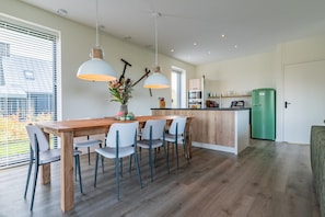 Eine moderne Küche mit einem Holztisch, weißen Stühlen, Pendelleuchten und einem grünen Kühlschrank.