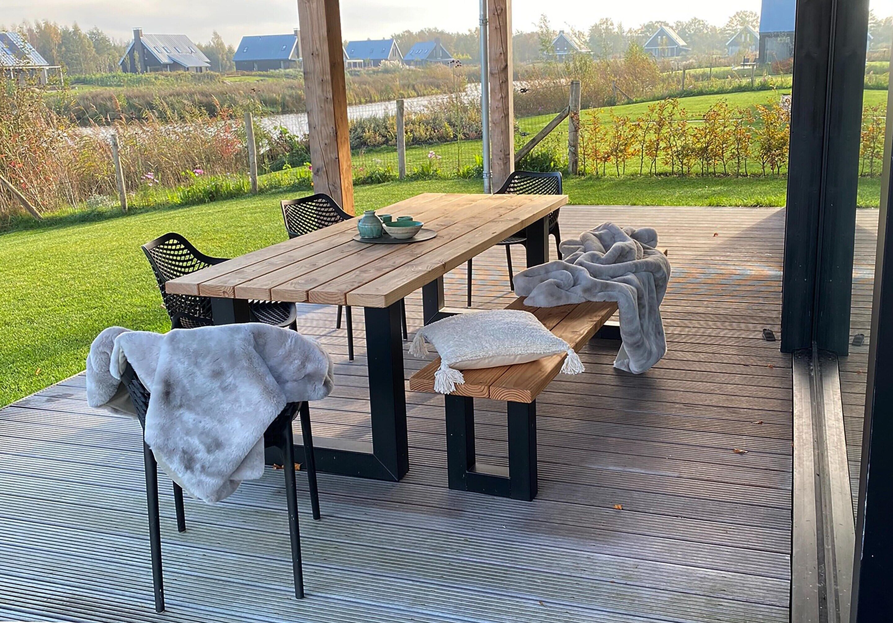 Una terraza al aire libre con una mesa y sillas de madera, un banco y vistas a un paisaje verde.