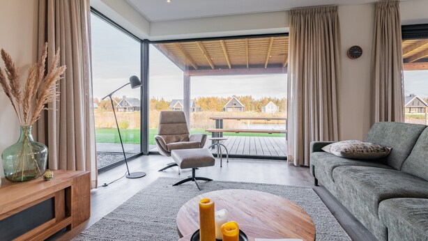 Una sala de estar moderna con un sofá, una mesa de centro, una lámpara y vistas a una terraza y casas.