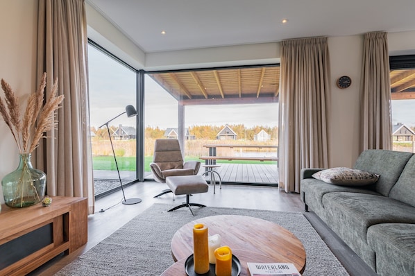 Ein modernes Wohnzimmer mit einer Couch, einem Couchtisch, einer Lampe und Blick auf eine Terrasse und Häuser.