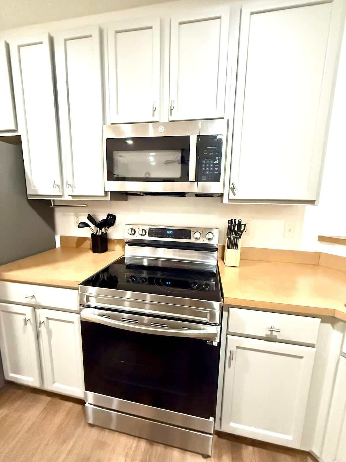 A kitchen with white cabinets, a microwave, an oven, and a countertop with utensils.
