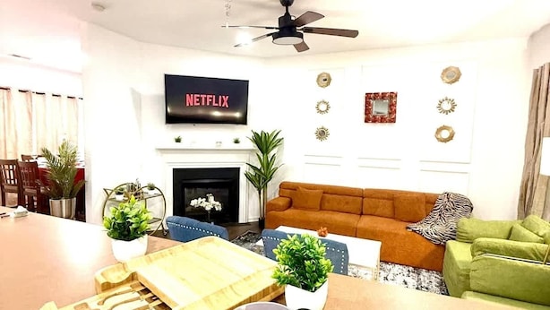 Un salon moderne doté d’un téléviseur à écran plat, d’une cheminée, d’un ventilateur de plafond et d’un coin repas avec une table et des chaises en bois.