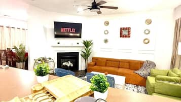 A modern living room with a flat-screen TV, a fireplace, a ceiling fan, and a dining area with a wooden table and chairs.