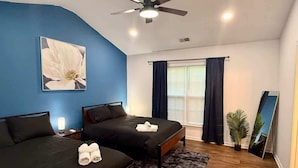 Une chambre avec deux lits, un ventilateur de plafond, une grande fenêtre avec des rideaux, un miroir et une plante en pot.