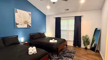 A bedroom with two beds, a ceiling fan, a large window with curtains, a mirror, and a potted plant.