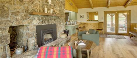 A stone fireplace, wooden ceiling, and a cozy seating area with a table and chairs.
