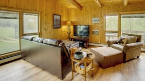 A wooden-paneled living room with a sofa, a chair, a television, and a fireplace.
