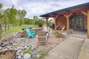 A covered patio area with outdoor seating, a grill, and a stone fire pit. - Mountain Views + Bbqs: Updated Cody Cabin (Cody)