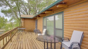 A wooden deck with a glass table and chairs, a covered seating area, and a view of trees.