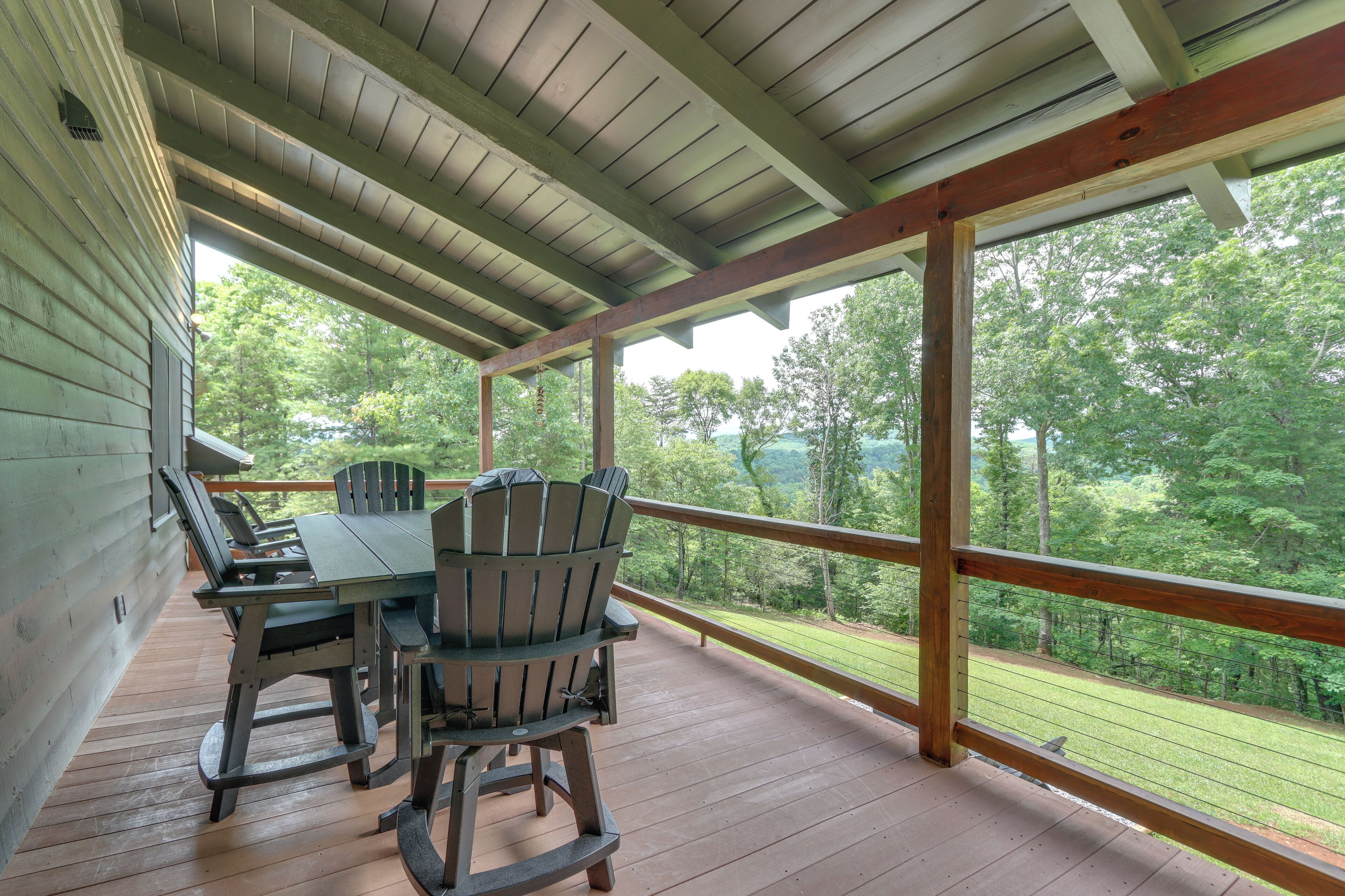 A covered outdoor deck with a table and chairs, overlooking a wooded area.