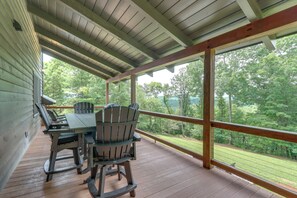 A covered outdoor deck with a table and chairs, overlooking a wooded area.