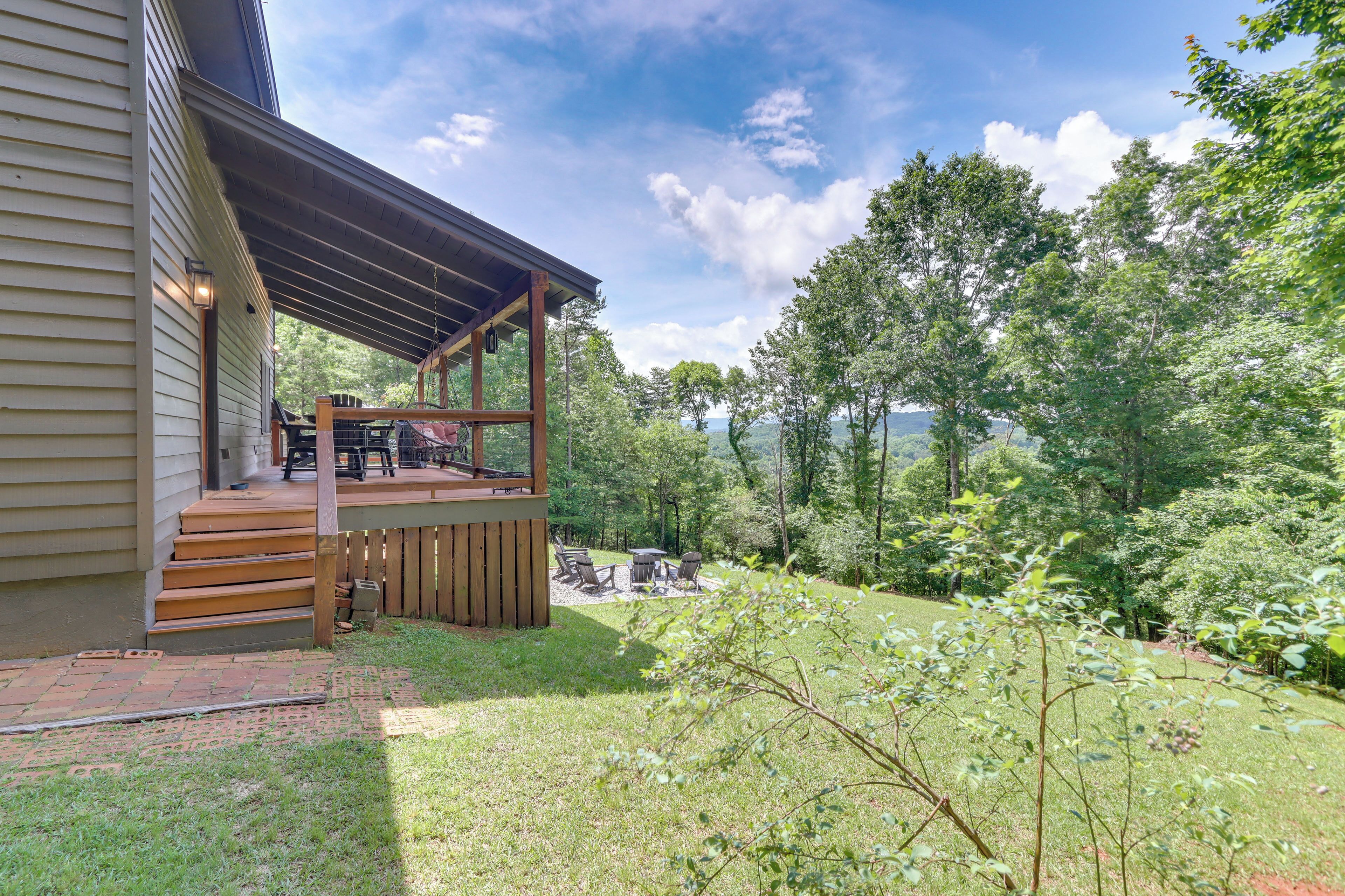 Un porche cubierto con mobiliario exterior, una terraza de madera y vistas a un área boscosa.