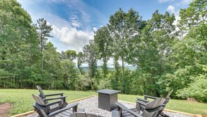 A deck with Adirondack chairs and a table, surrounded by a gravel area with a view of a forest and mountains.
