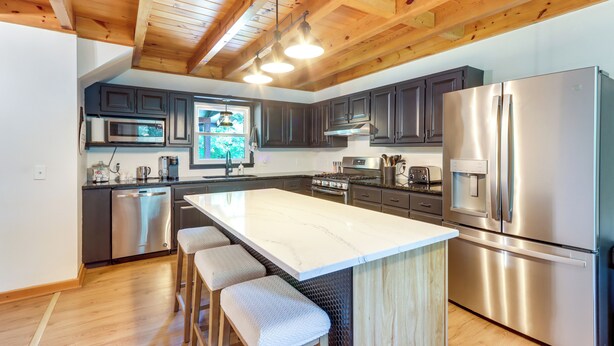 A modern kitchen with a large island, stainless steel appliances, and wooden ceiling beams.