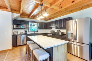 A modern kitchen with a large island, stainless steel appliances, and wooden ceiling beams.