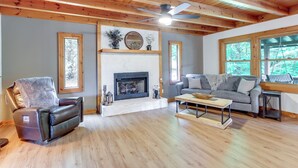 A living room with a fireplace, a leather recliner, a gray sofa, and wooden flooring.