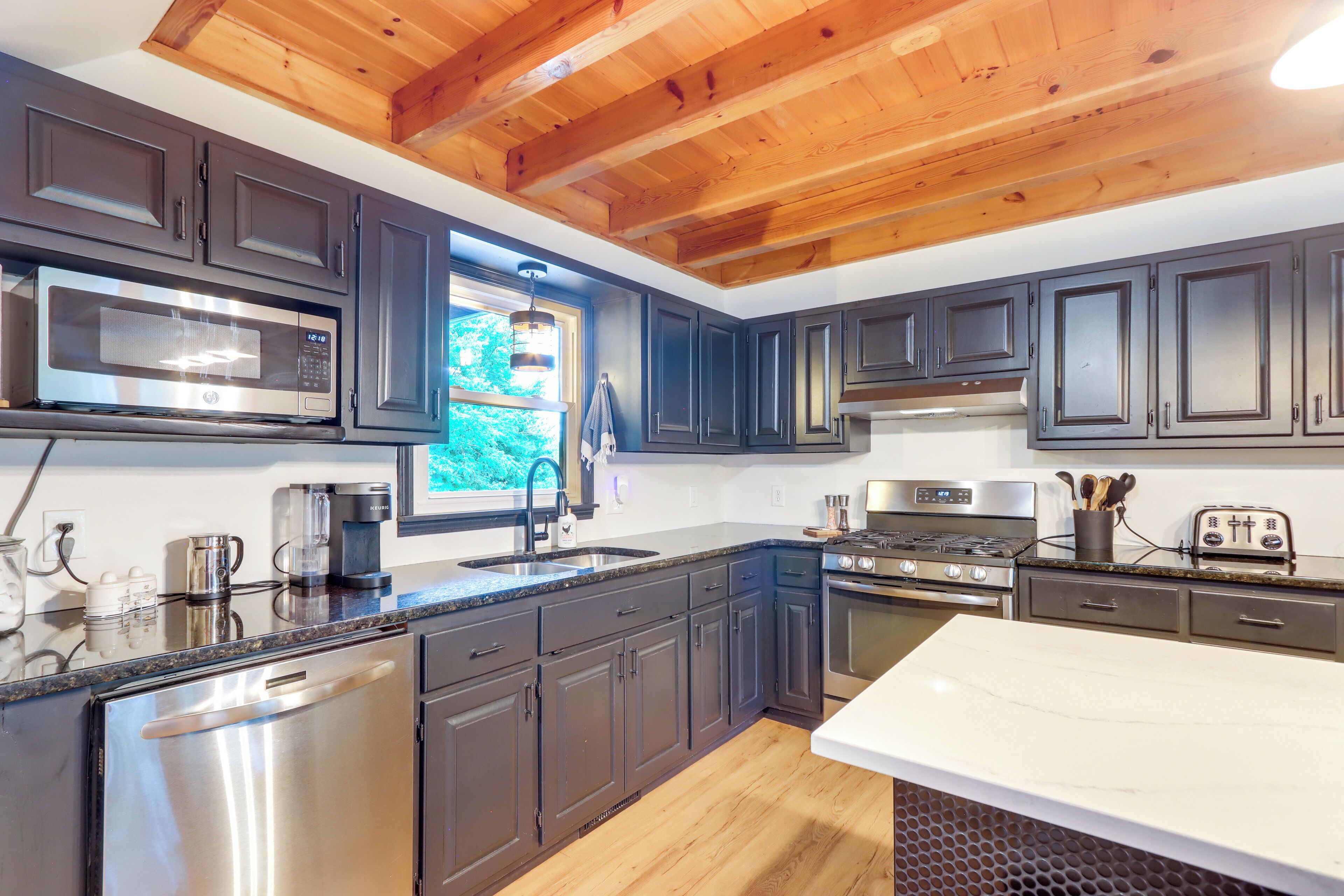 A modern kitchen with dark cabinets, stainless steel appliances, and a wooden ceiling.