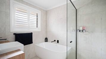 Ein modernes Badezimmer mit freistehender Badewanne, einer Glasdusche und einem Fenster mit Jalousien.