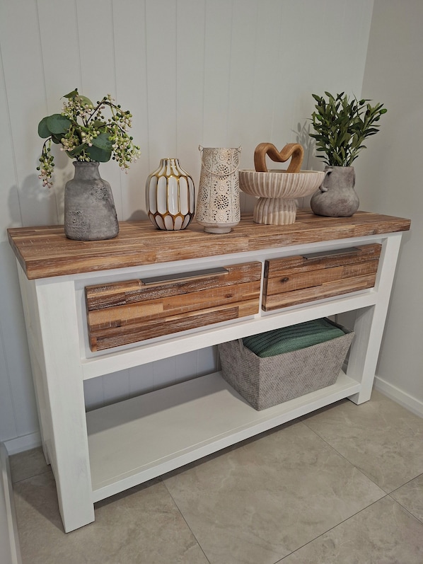 A white console table with a wooden top, three vases, and two plants.