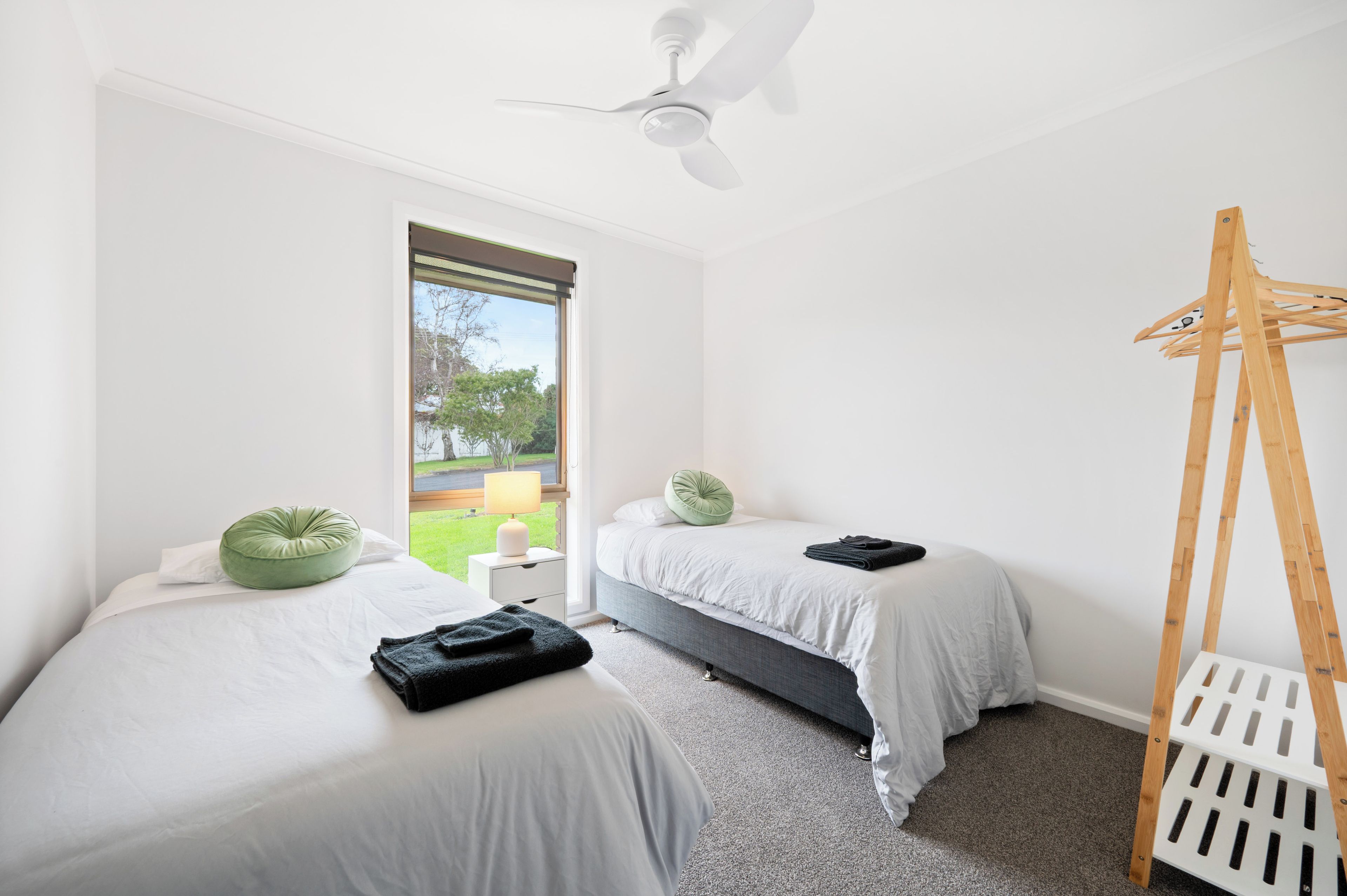 Une chambre avec deux lits, un ventilateur de plafond, une fenêtre donnant sur un paysage verdoyant et une échelle en bois.