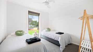 Une chambre avec deux lits, un ventilateur de plafond, une fenêtre donnant sur un paysage verdoyant et une échelle en bois.