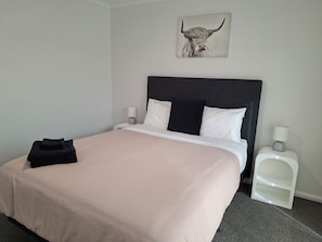 A neatly made bed with a pink bedspread, two pillows, a black pillow, and a wall-mounted picture of a bull.