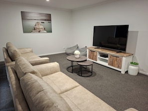 A living room with a sectional sofa, a TV on a wooden stand, a small round table, and a painting on the wall.
