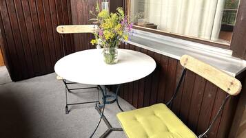 Una mesa redonda con un florero, una silla con cojín y una ventana con cortinas.