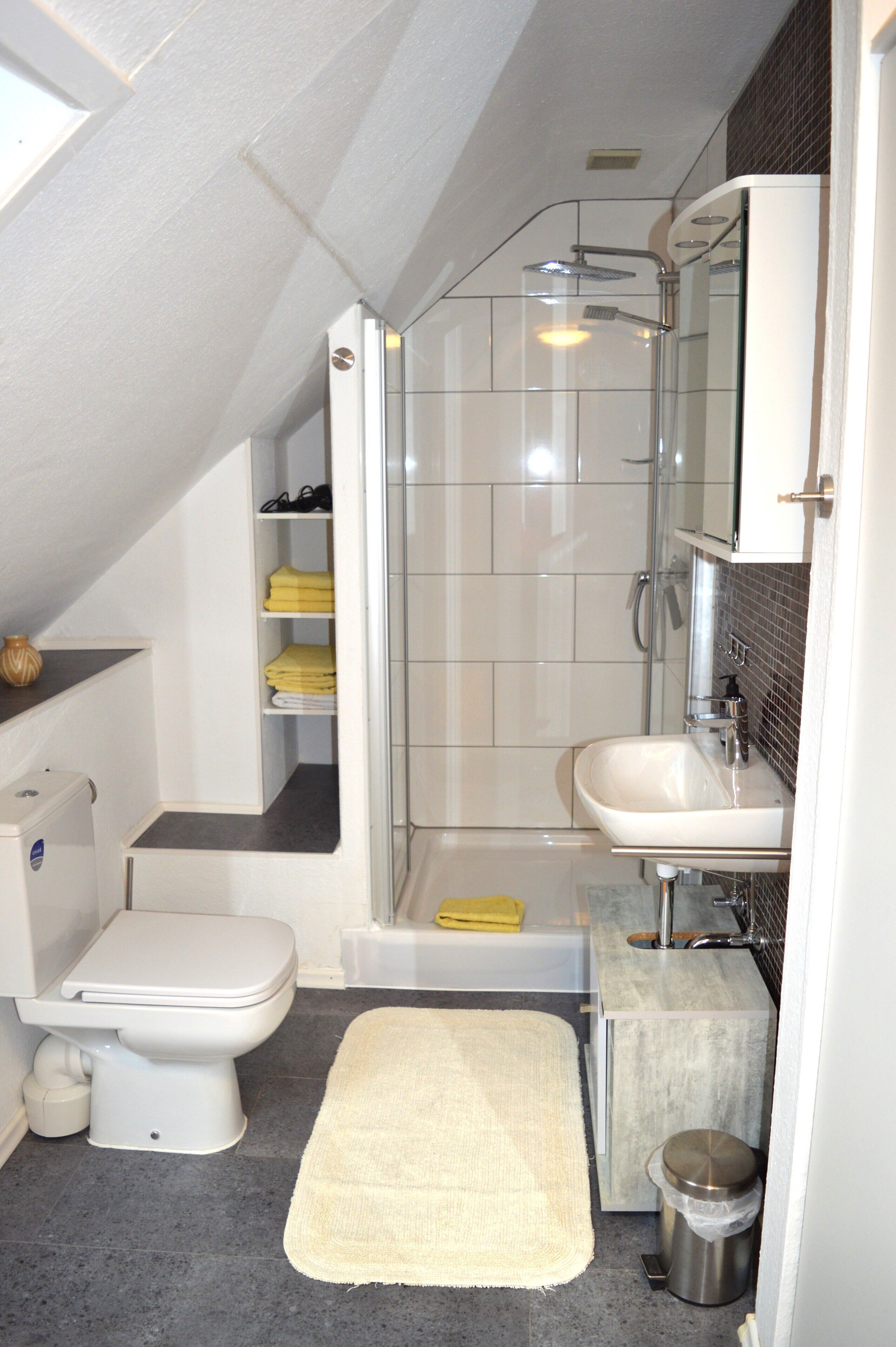 Ein kleines Badezimmer mit Toilette, Waschbecken, Dusche und Ablageflächen.