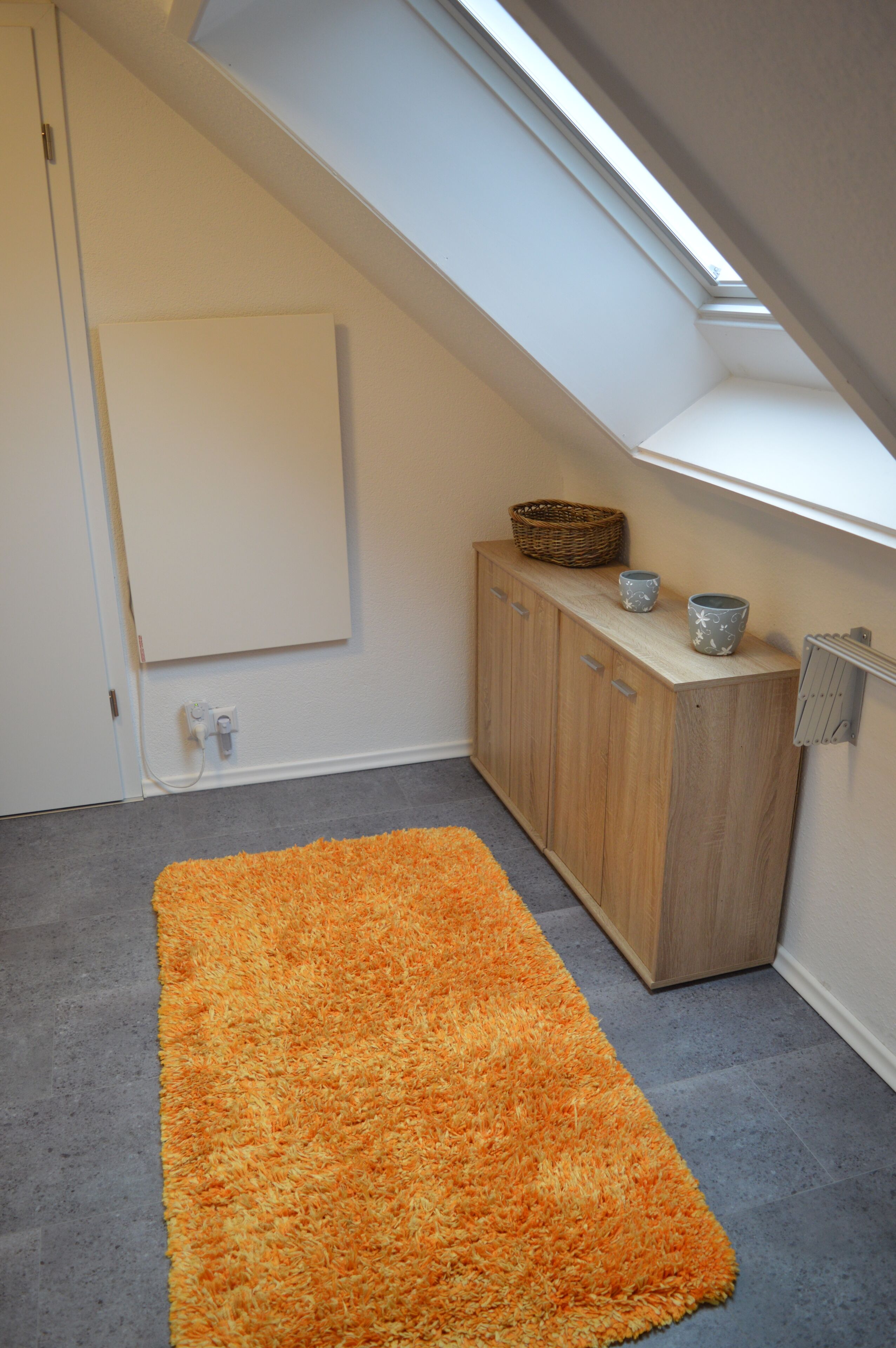 Une pièce dotée d’une lucarne, d’une armoire en bois et d’un tapis gris.